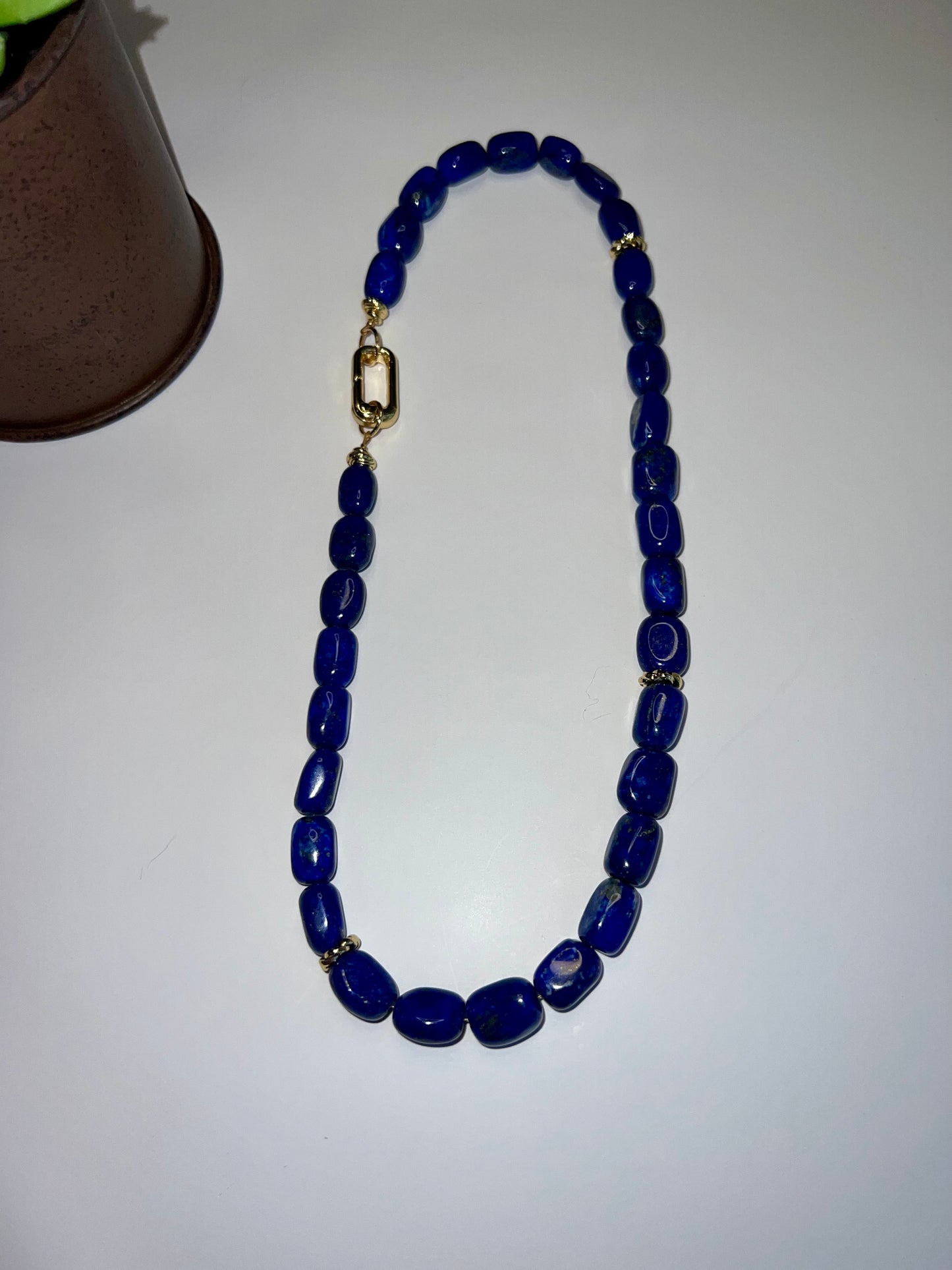 a blue beaded necklace on a table next to a cup