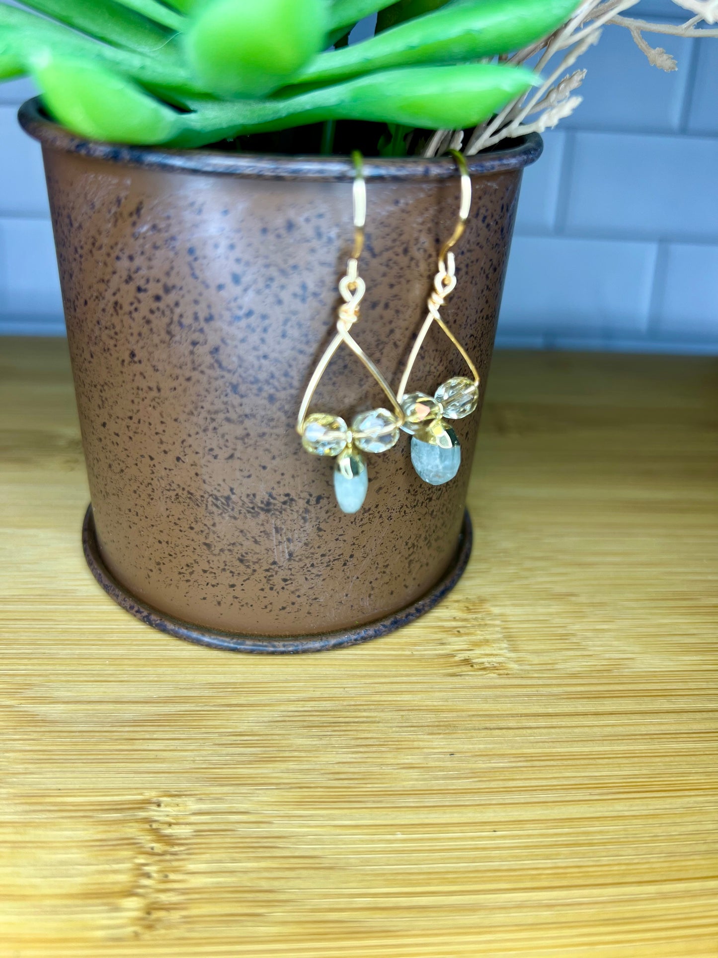 A pair of gold earrings with green stones hanging from them, displayed in a brown vase on a wooden surface.