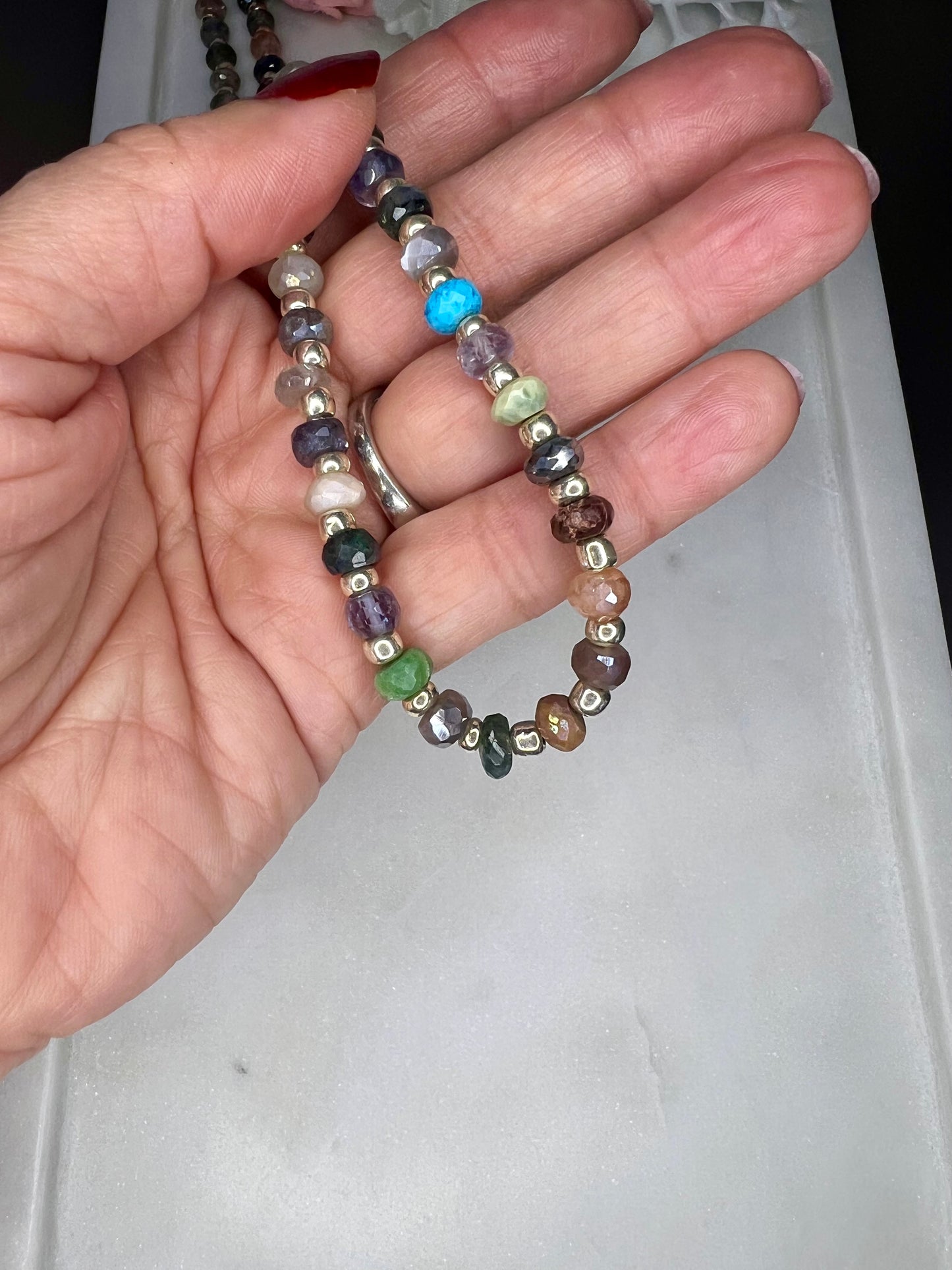 A hand is holding a colorful beaded bracelet with various colored beads, including silver, blue, green, and brown.