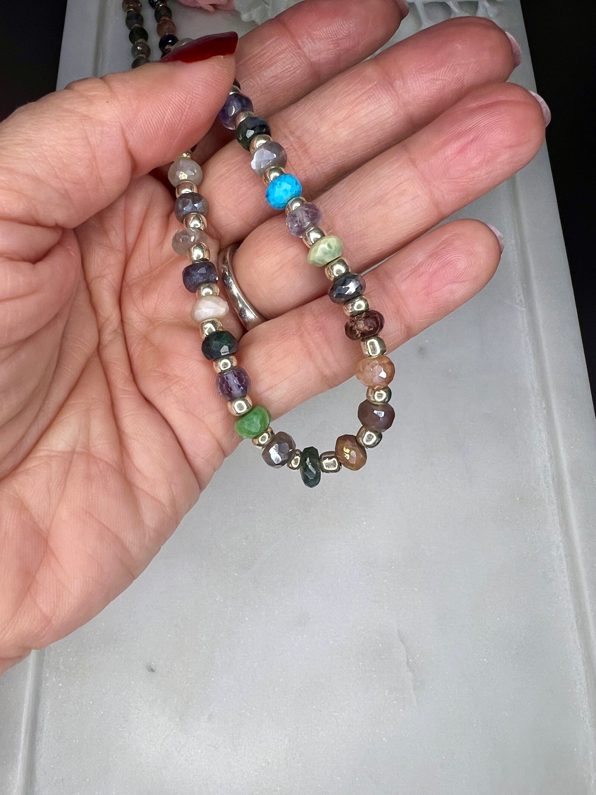 A hand is holding a colorful beaded bracelet with various colored beads, including silver, blue, green, and brown.