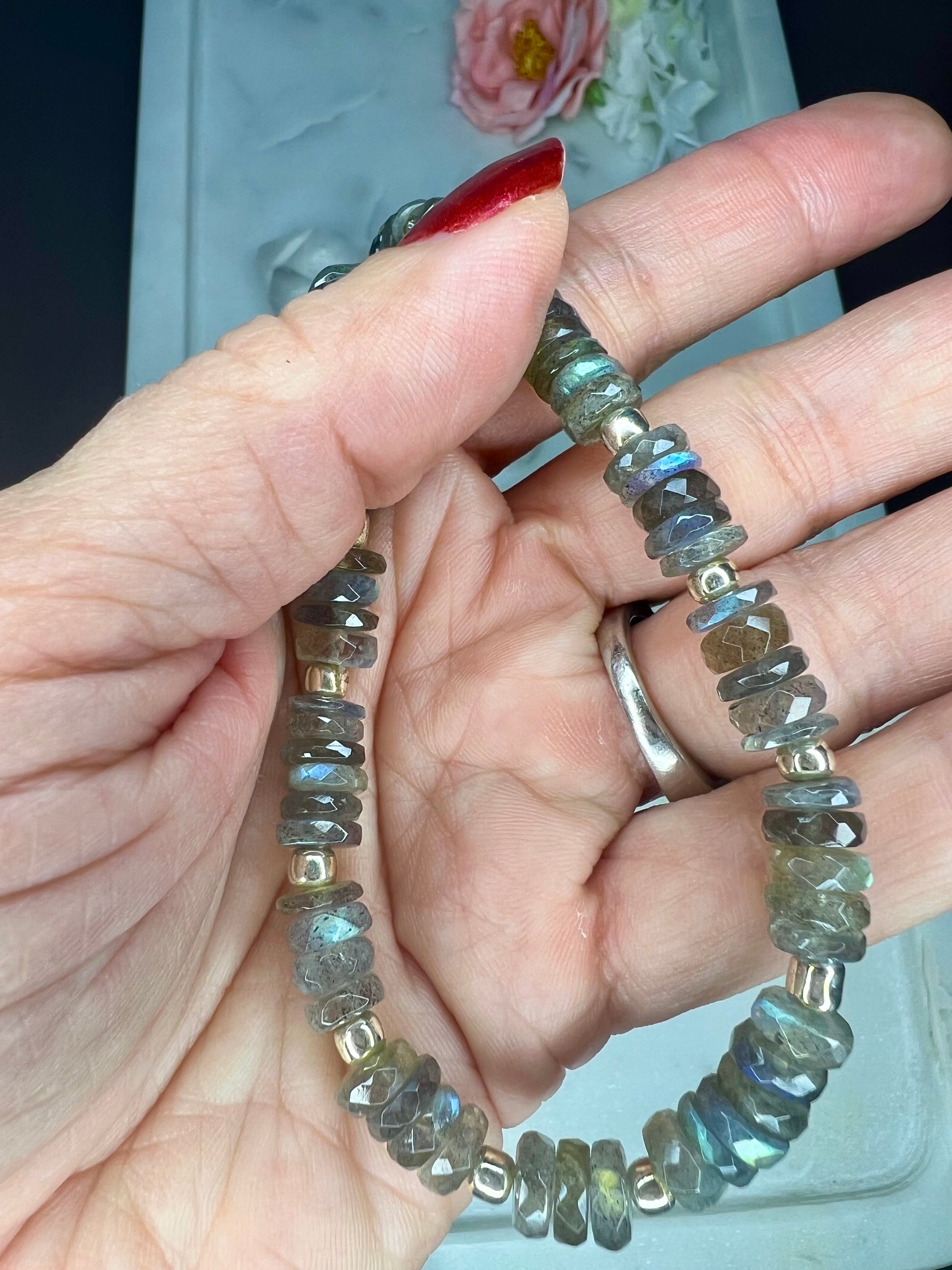 A hand is holding a bracelet made of small, multicolored beads.