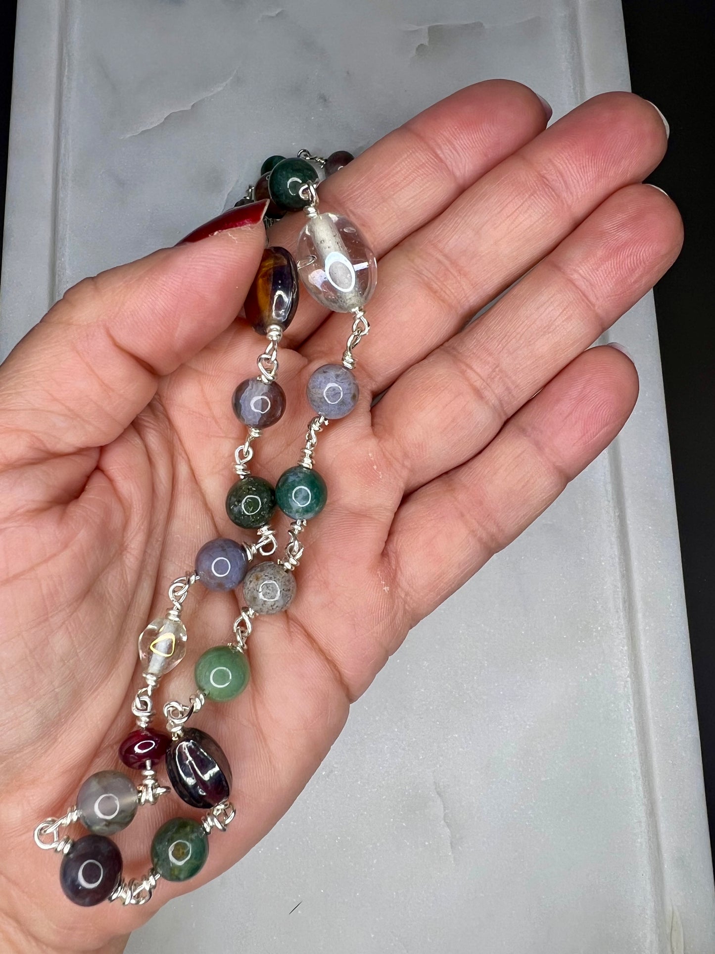 A hand holding a colorful beaded necklace against a white background.