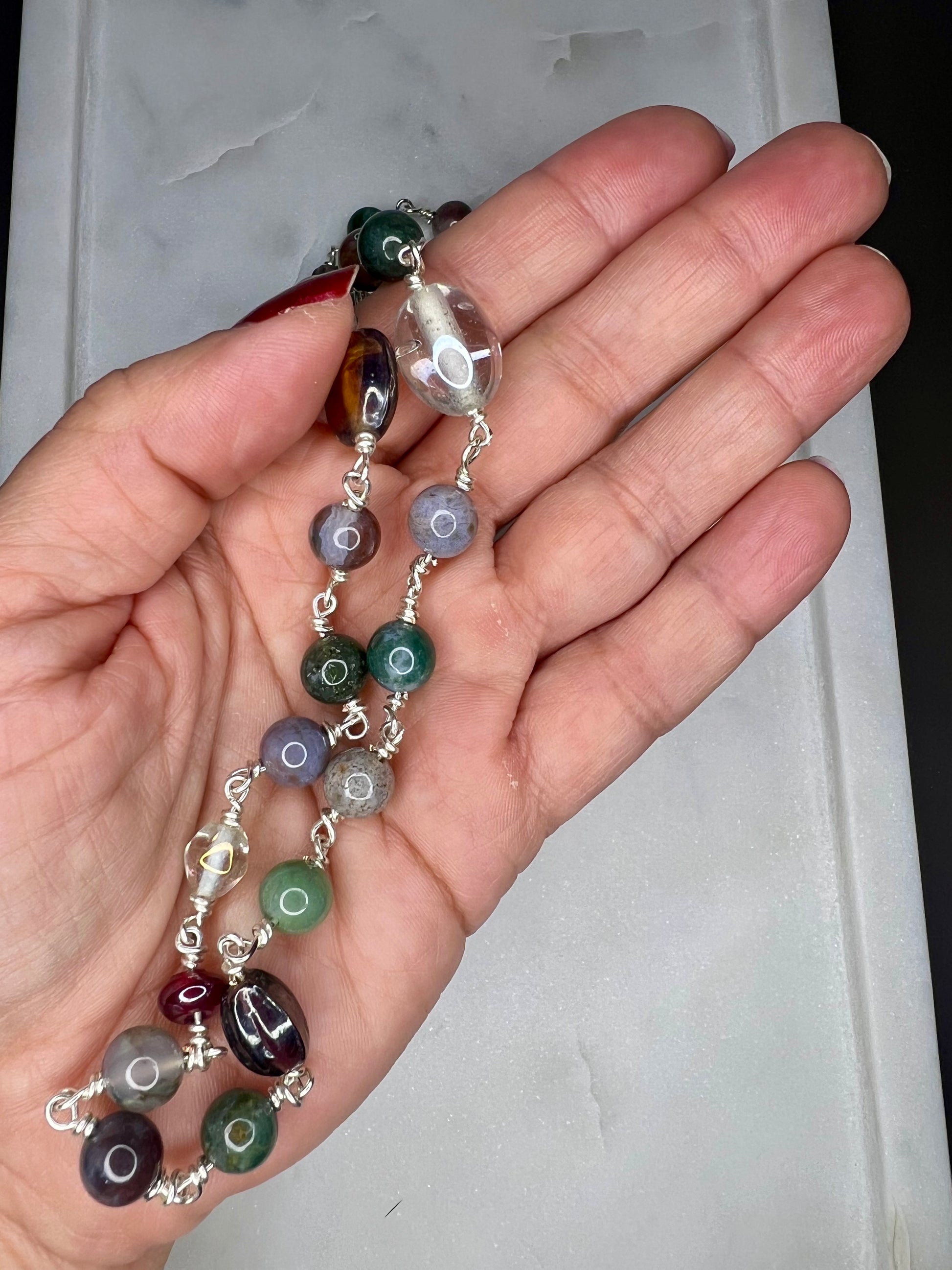 A hand holding a colorful beaded necklace against a white background.