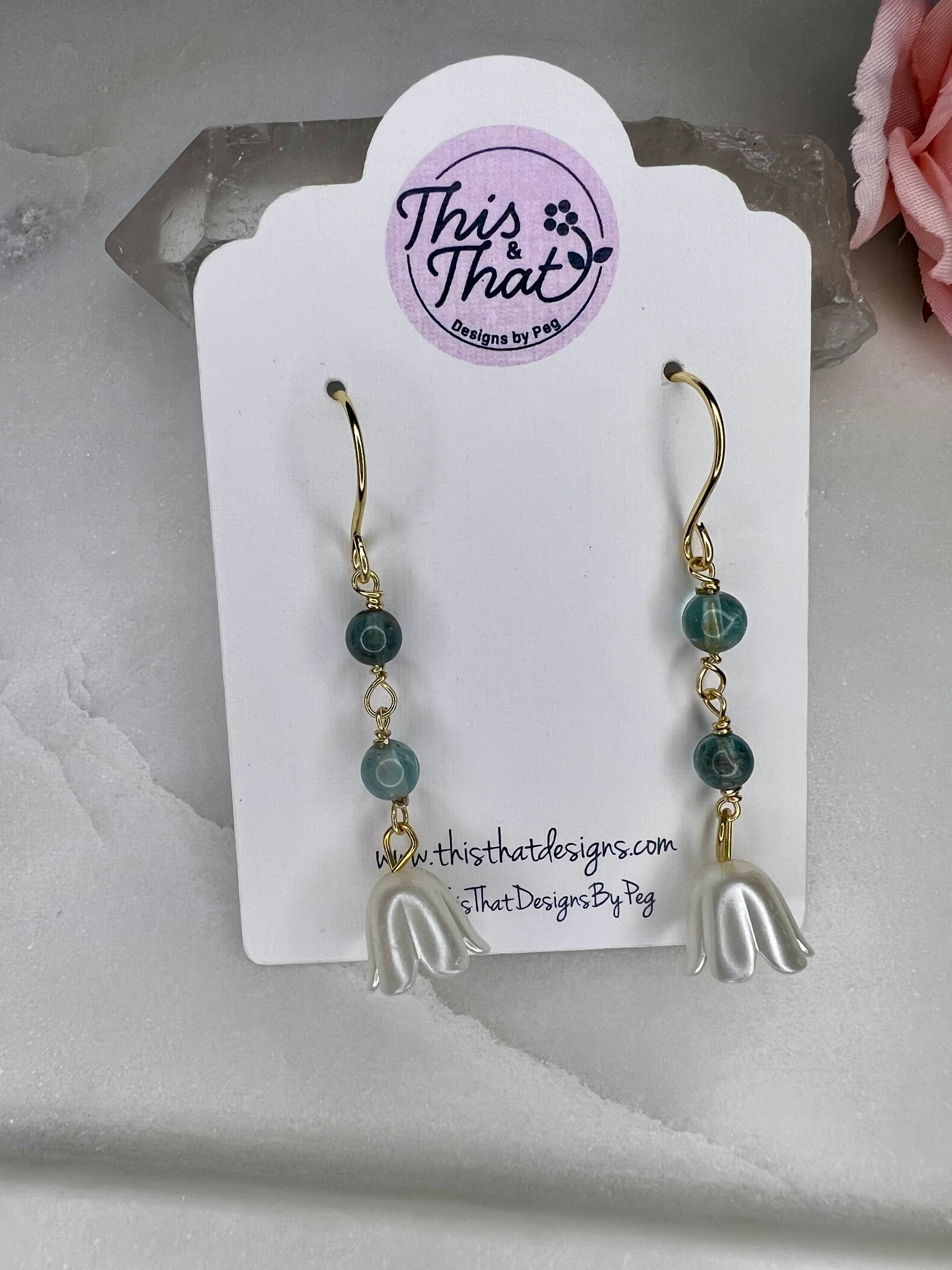 This image shows a pair of earrings with a floral design, displayed on a white card with a website address.