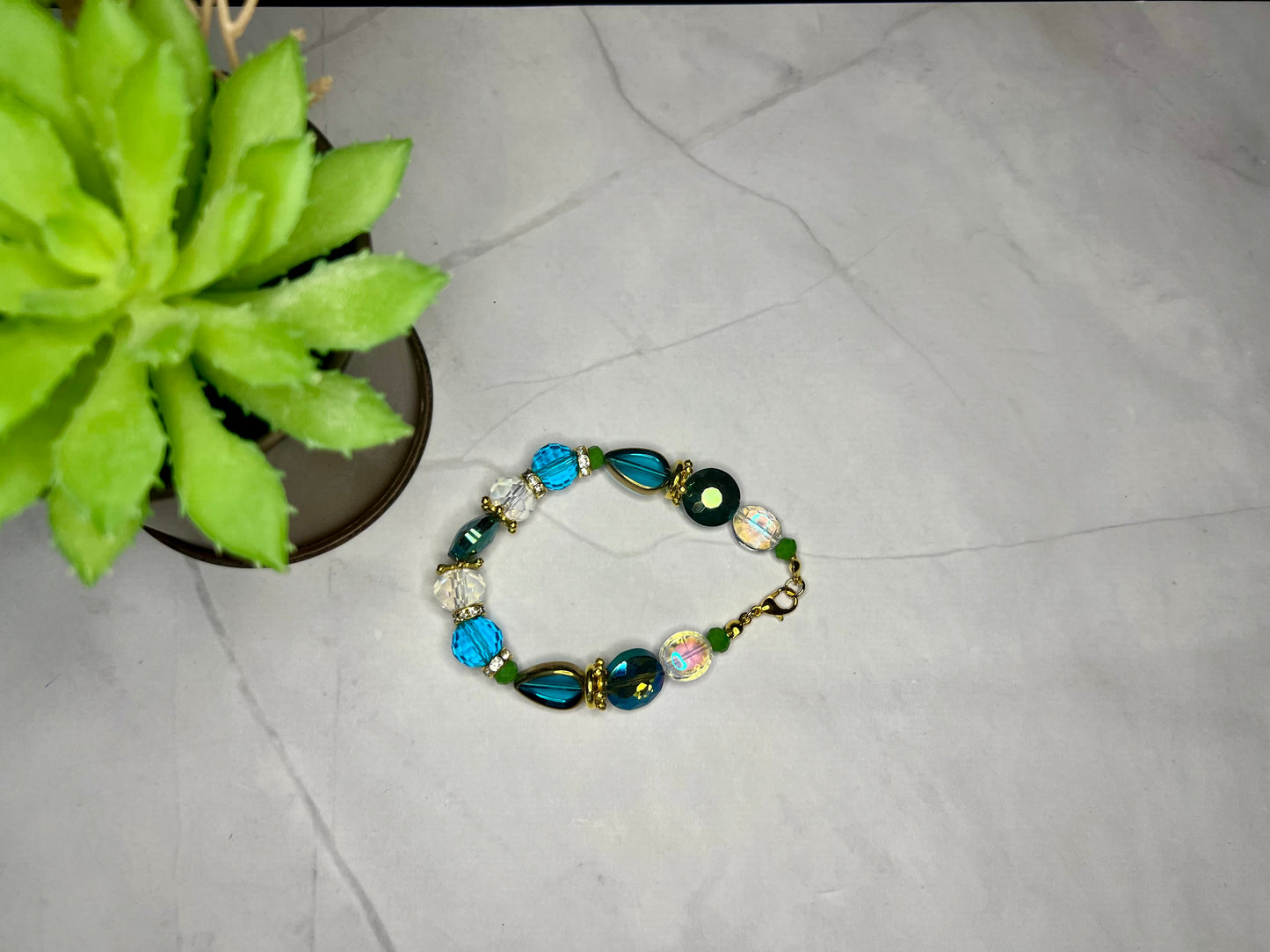 a blue and green beaded bracelet next to a potted plant