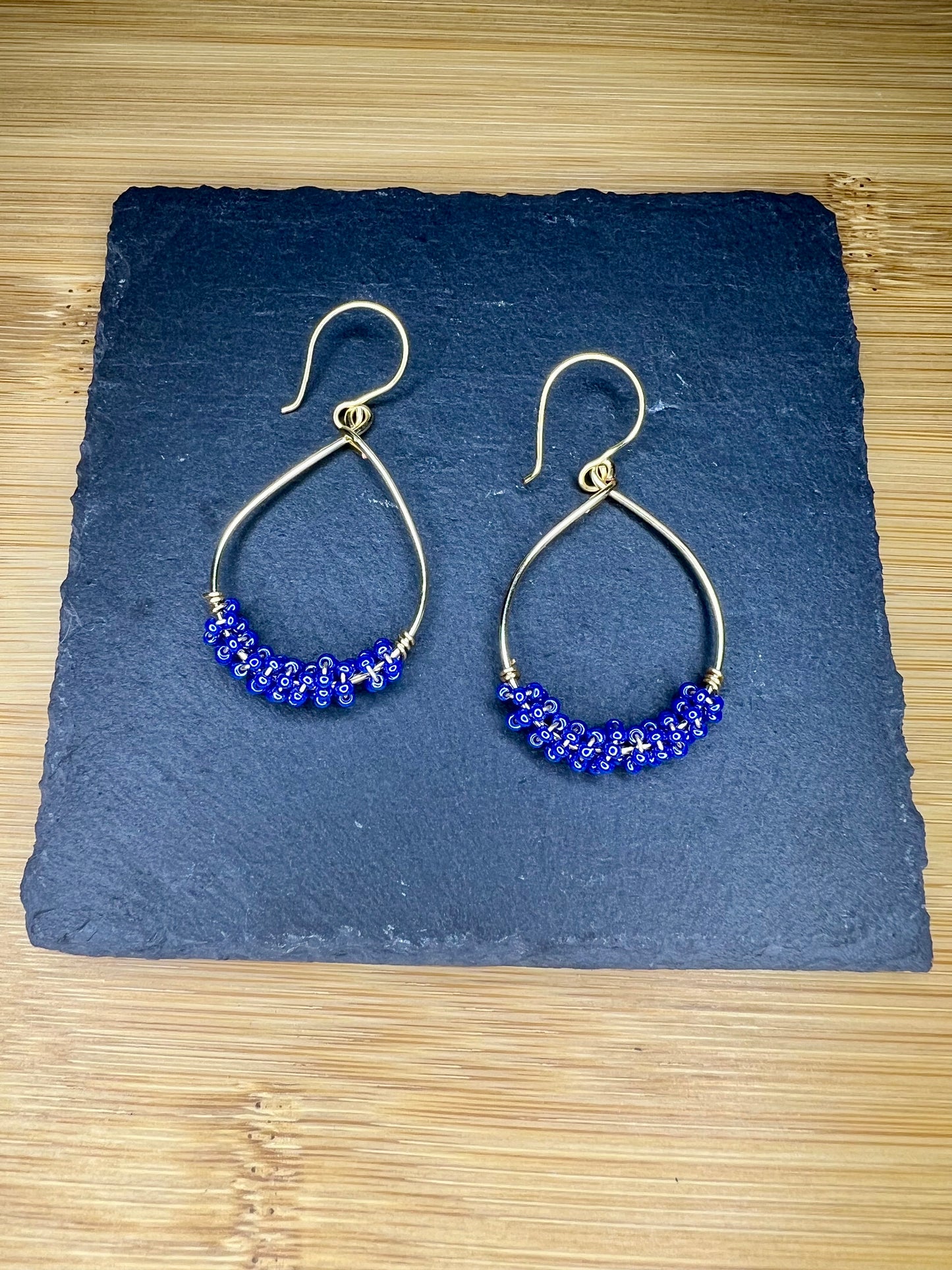 A pair of gold hoop earrings with blue beads, displayed on a dark slate surface.