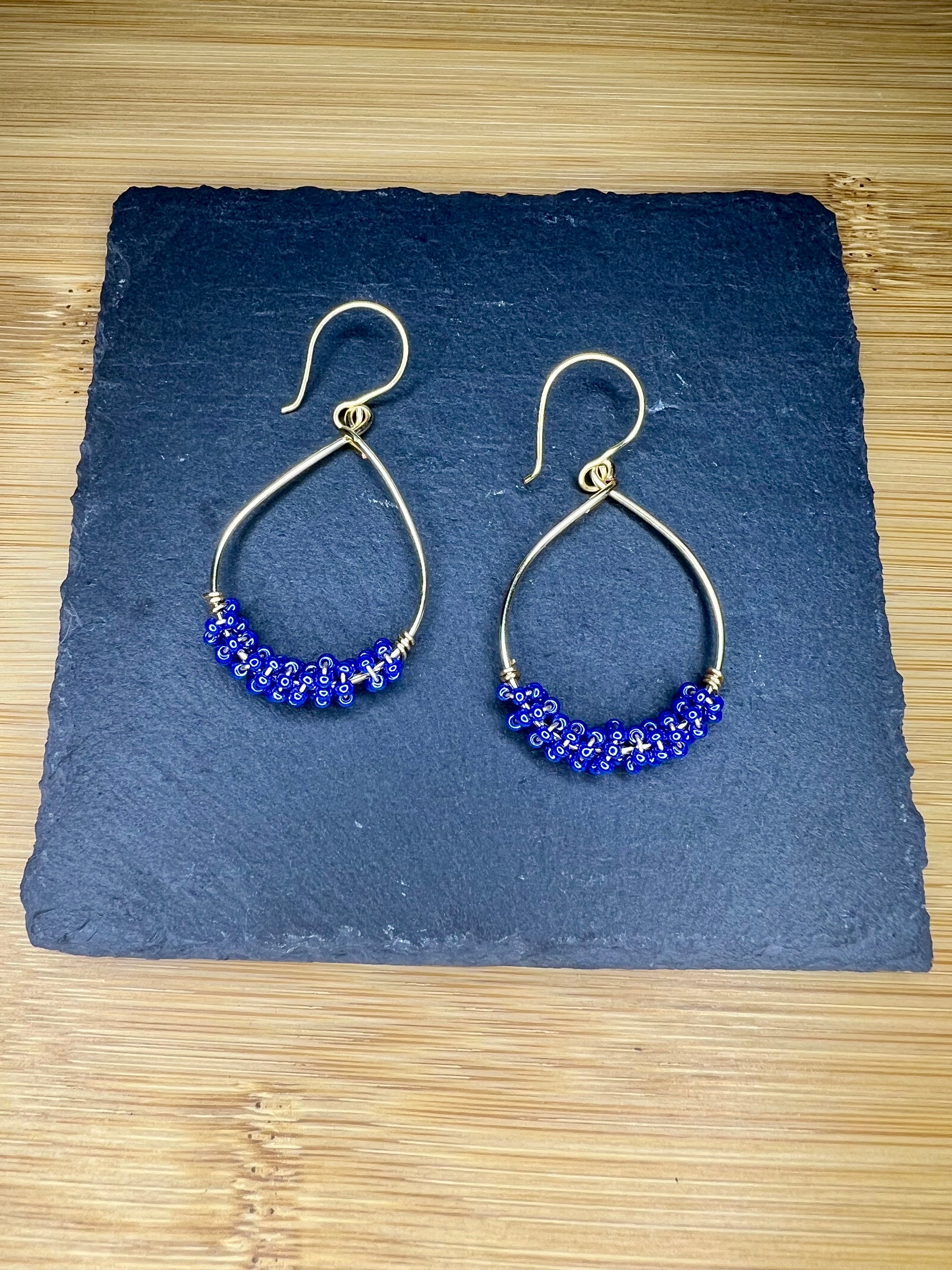 A pair of gold hoop earrings with blue beads, displayed on a dark slate surface.