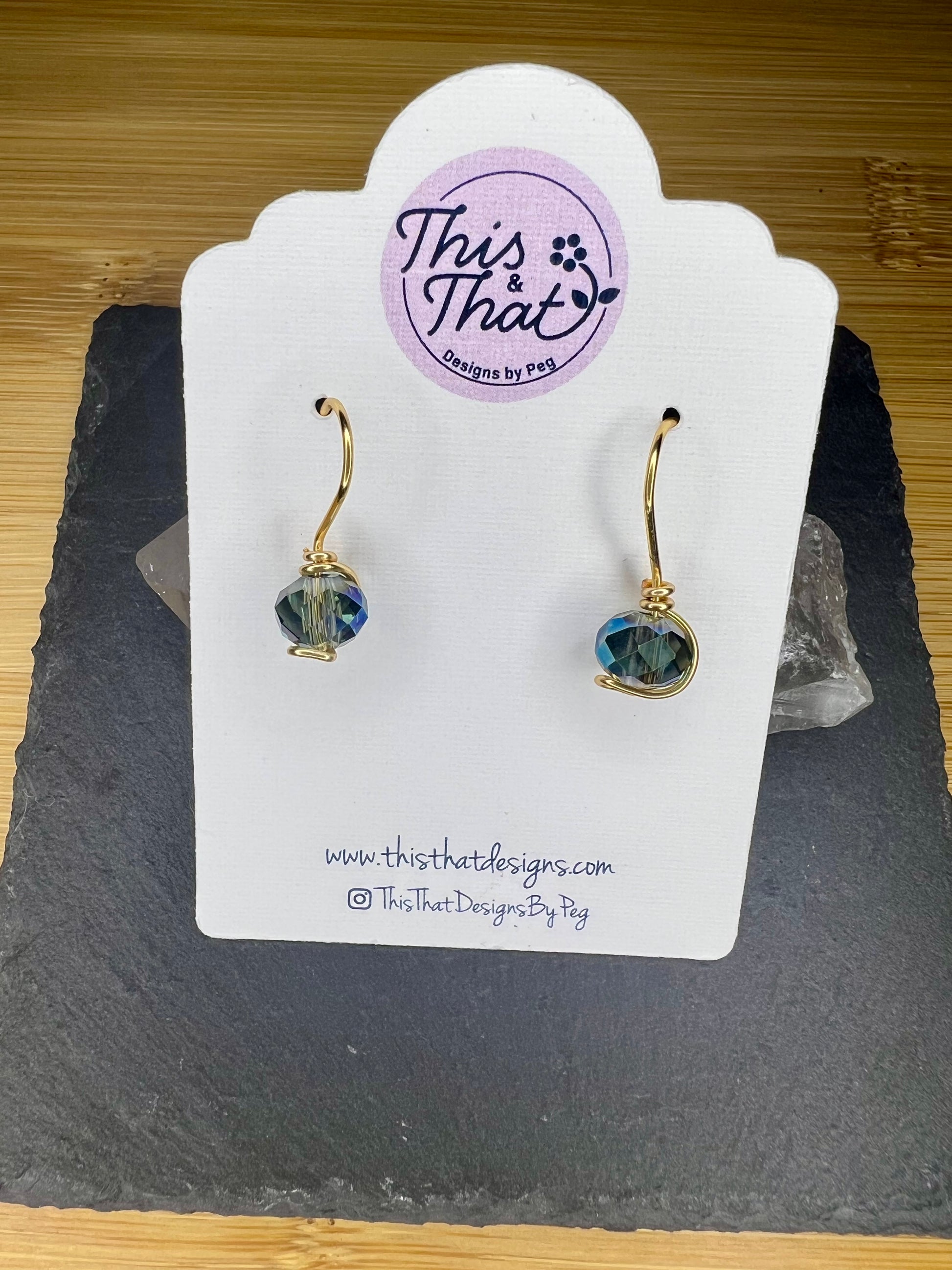 a pair of earrings displayed on a white card with a website address and a logo.