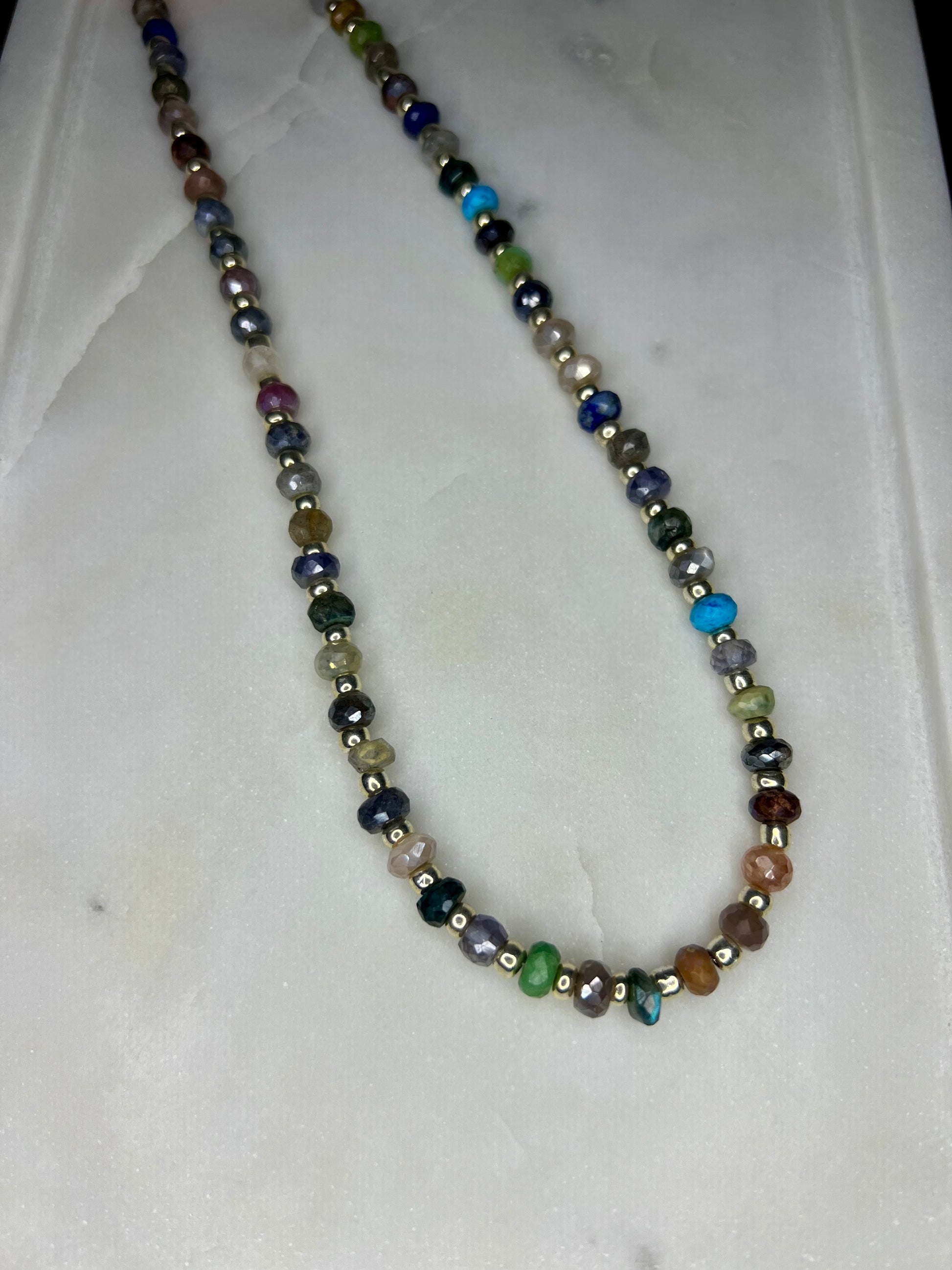 A colorful beaded necklace with various colored beads, including silver, blue, green, and brown, arranged in a row.