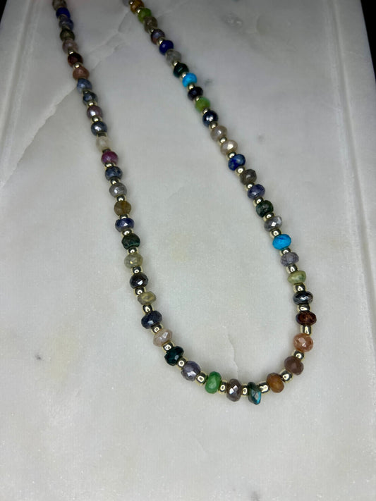 A colorful beaded necklace with various colored beads, including silver, blue, green, and brown, arranged in a row.