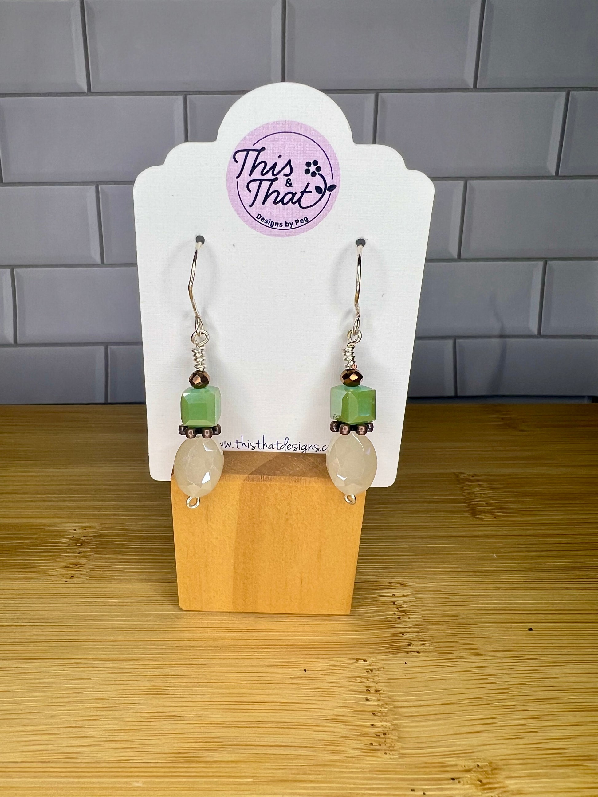 A pair of earrings with green and white stones hanging from them, displayed on a wooden stand.