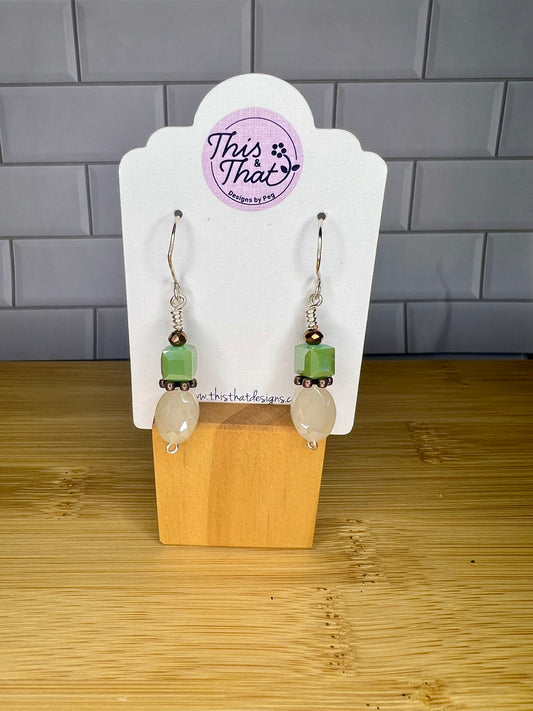 A pair of earrings with green and white stones hanging from them, displayed on a wooden stand.