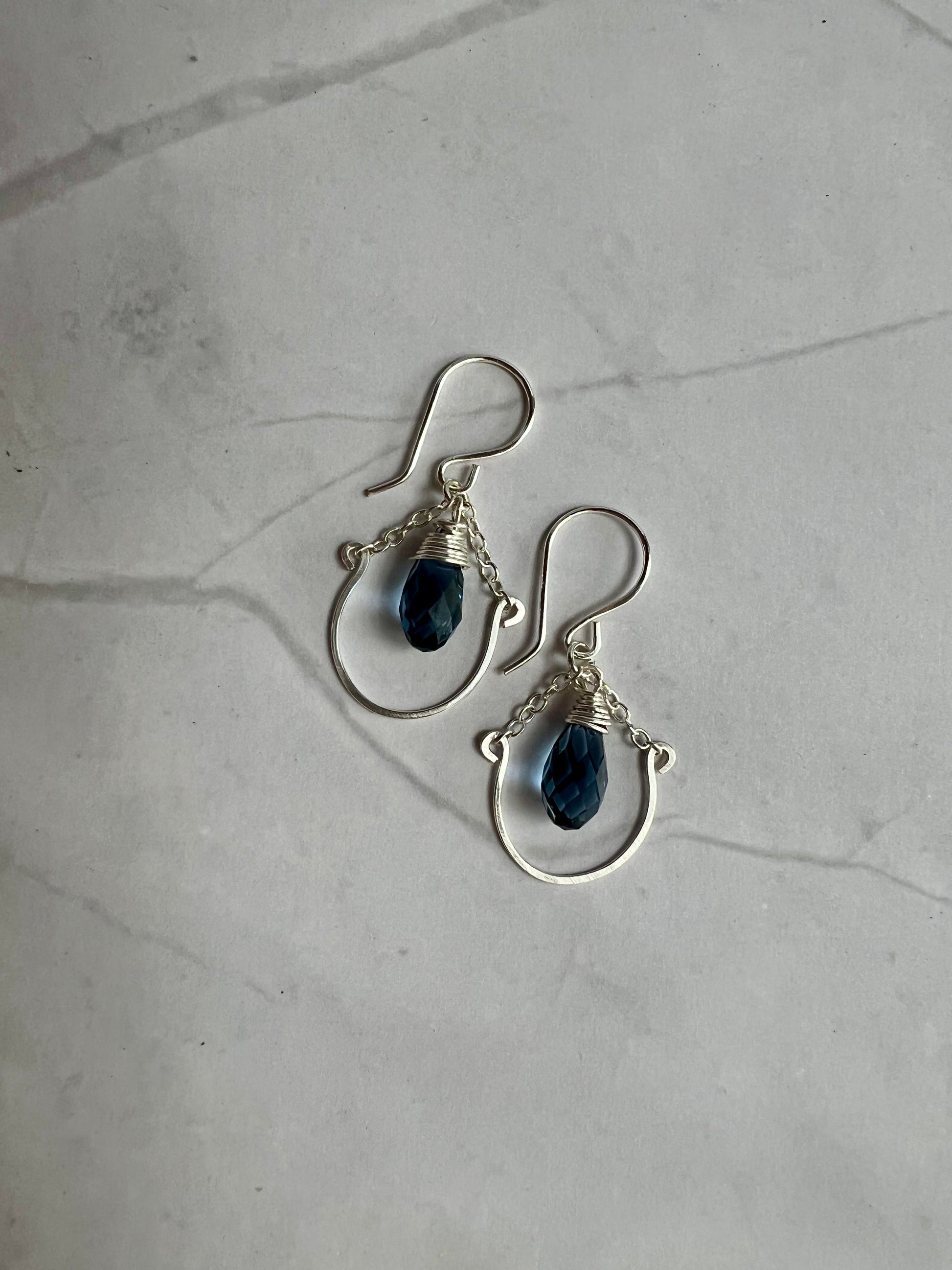 A pair of silver earrings with blue gemstones hanging from the hooks.