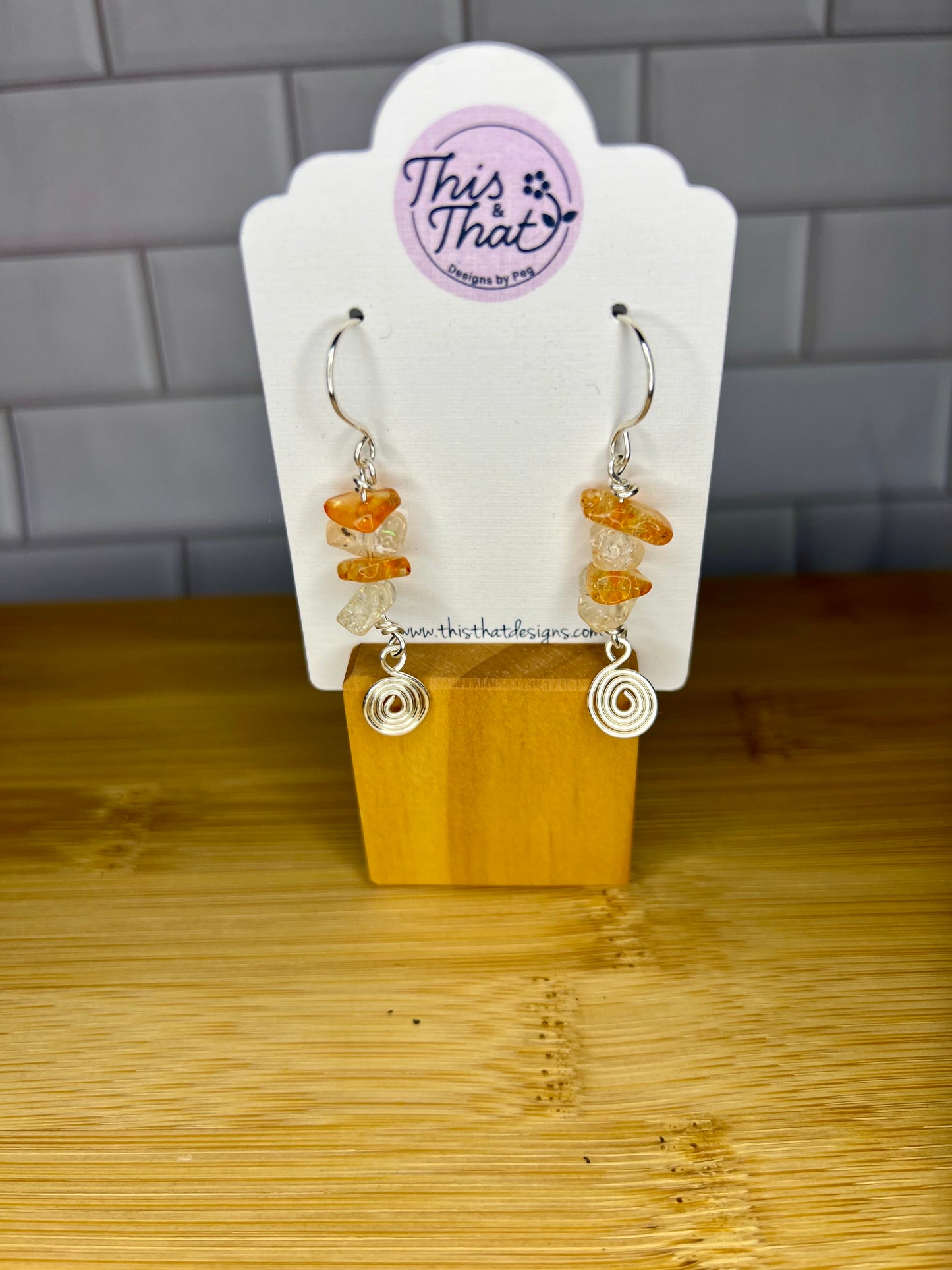 A pair of earrings with a wooden stand and a white card displaying the brand name and product details.